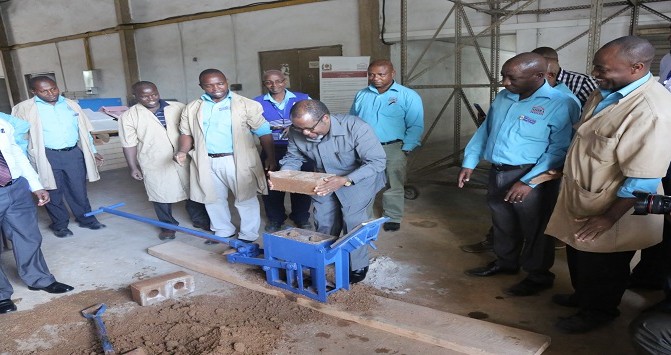 Katibu Mkuu Kiongozi Mstaafu Balozi Ombeni Sefue akitoa tofali la kufungamana kwenye mashine alipotembelea ofisi ya Wakala wa Taifa wa Utafiti wa Nyumba Bora na Vifaa vya Ujenzi 